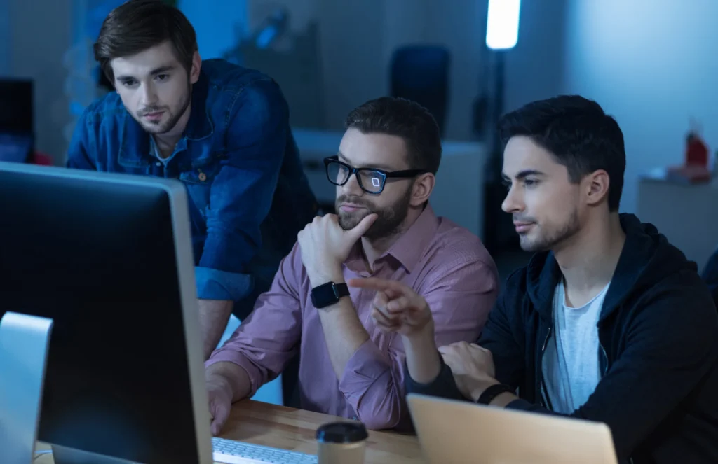 Trois développeurs concentrés devant un écran d'ordinateur, discutant et collaborant sur un projet.